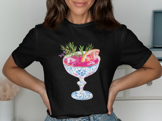 Black t-shirt featuring a pink cocktail in a decorative glass garnished with citrus and herbs.