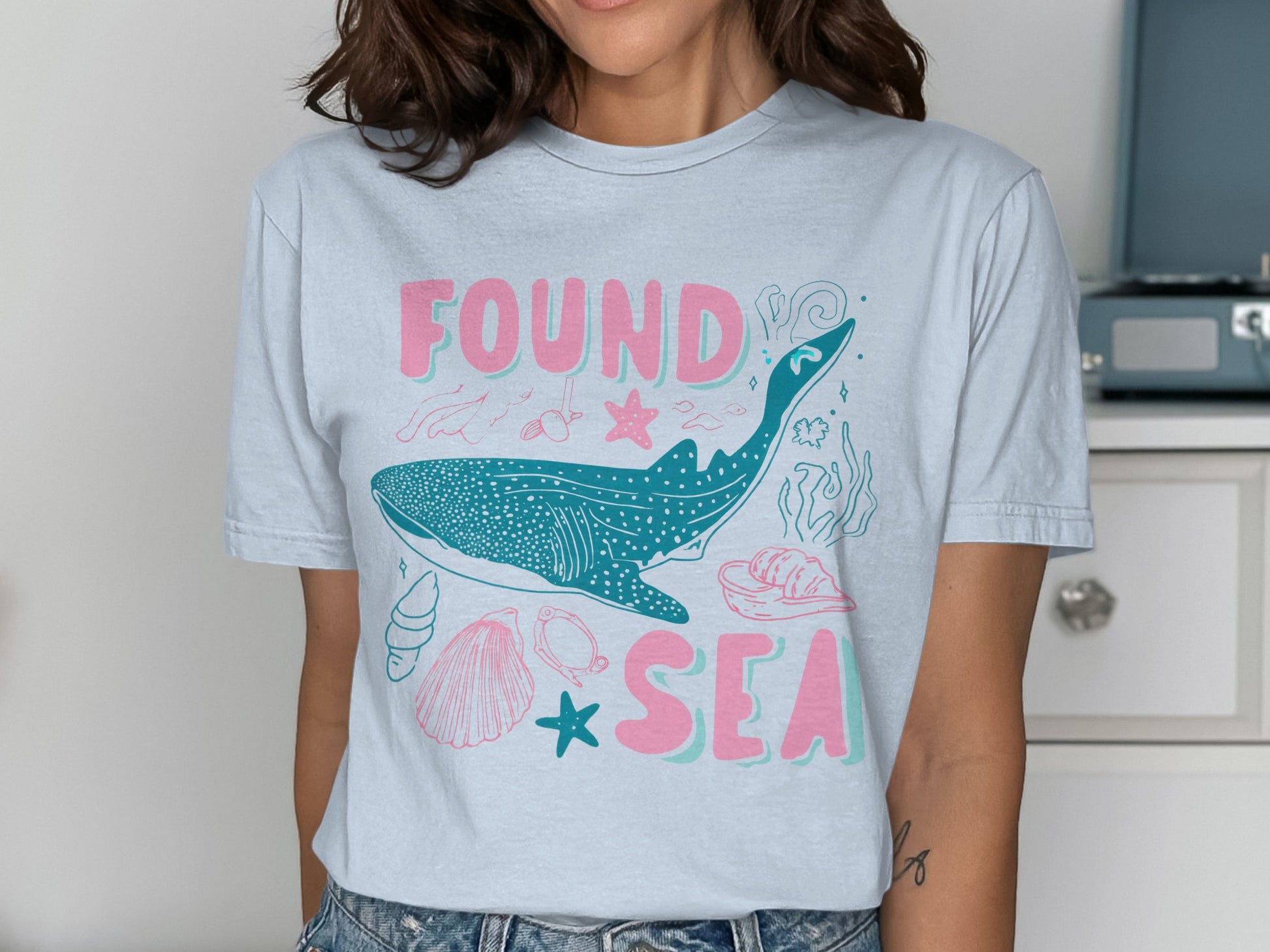 Light blue t-shirt with whale, seashells, and text "FOUND SEA".