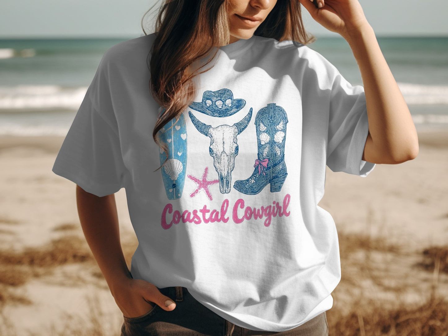 White t-shirt with "Coastal Cowgirl" text and cowboy boots, skull, and surfboard graphics.