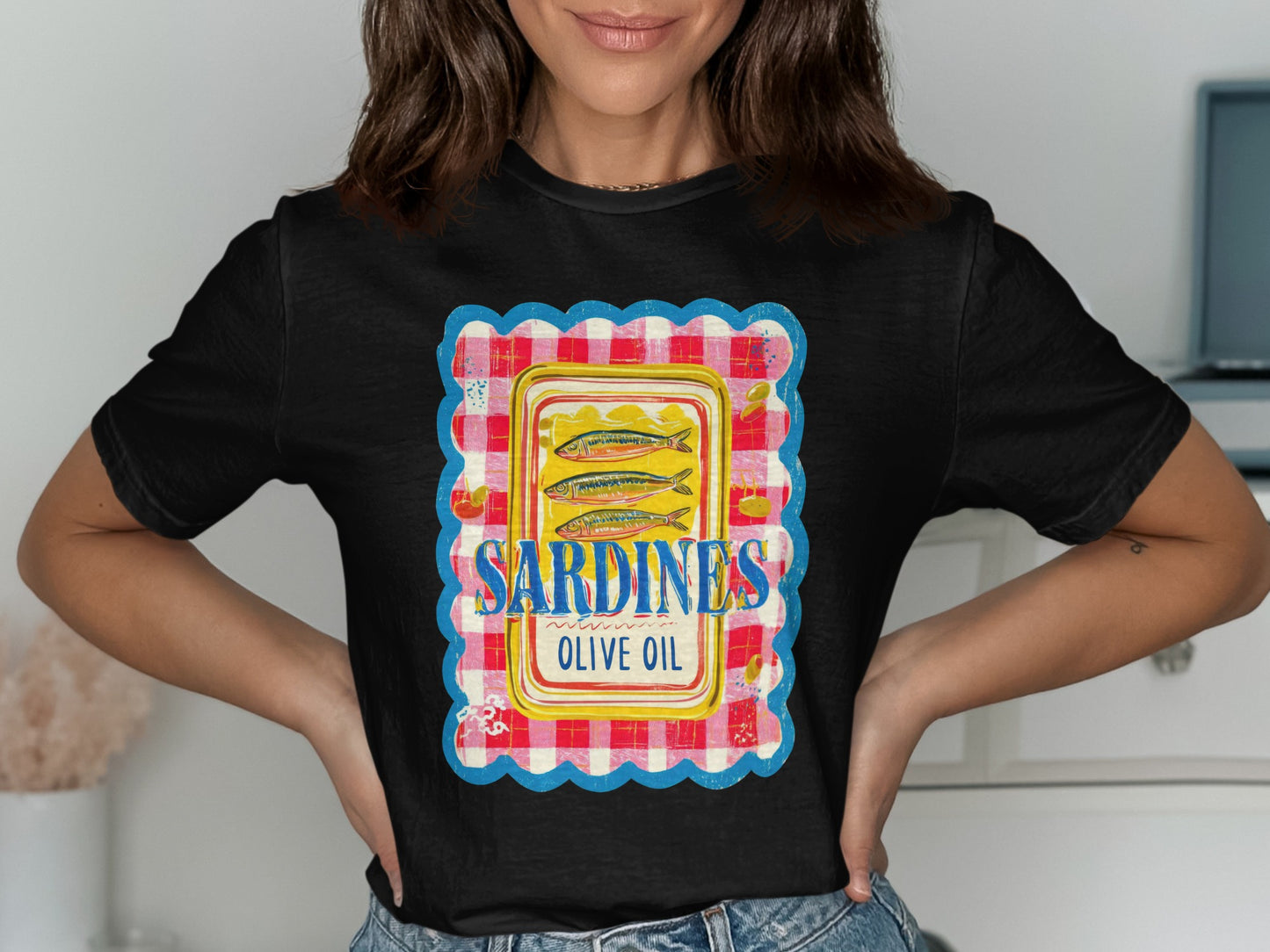 Black t-shirt with a graphic of three sardines in olive oil on a red and white checkered background.