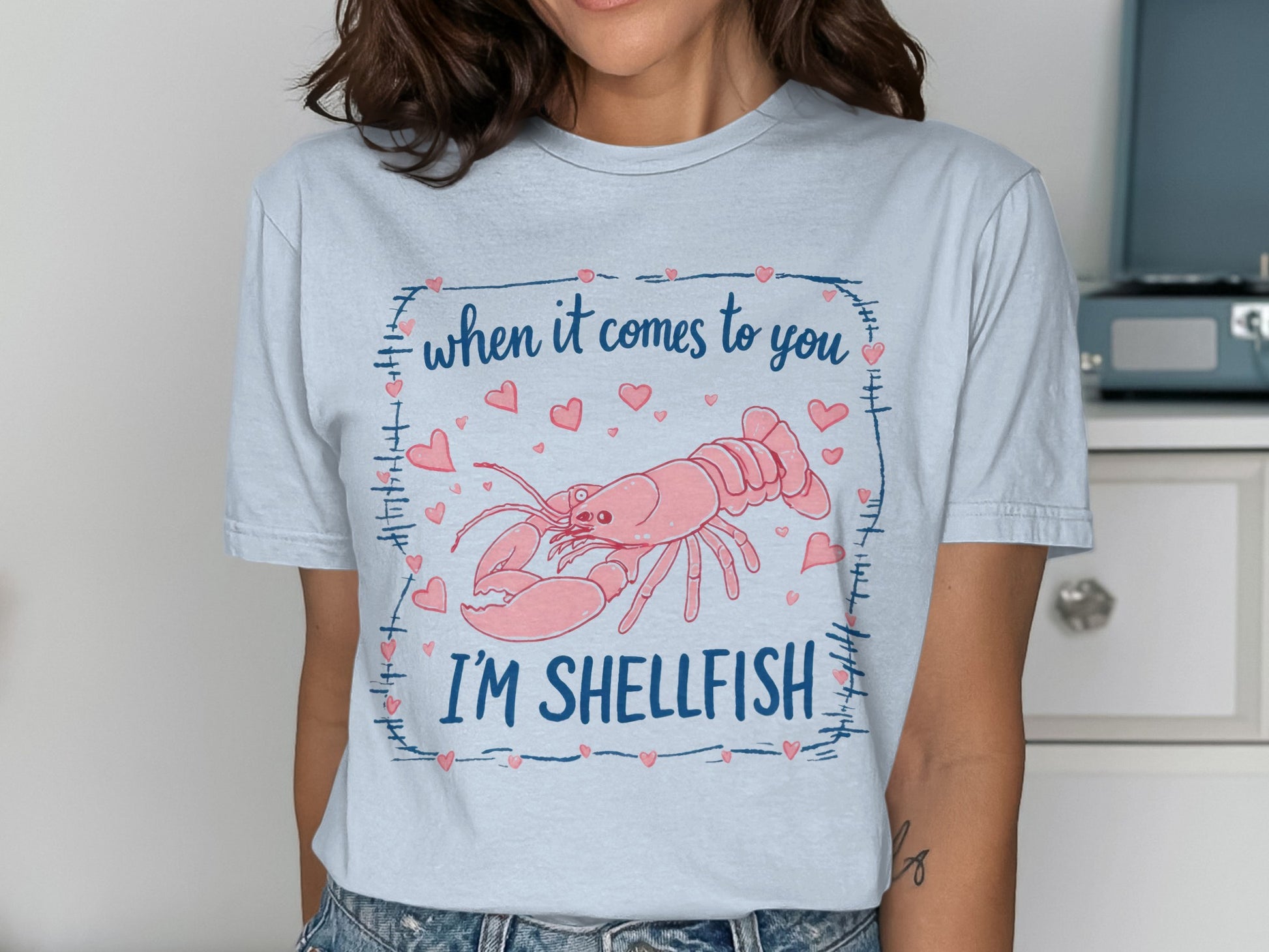 Light blue t-shirt with a pink lobster and hearts, text reads "When it comes to you, I'm SHELLFISH".