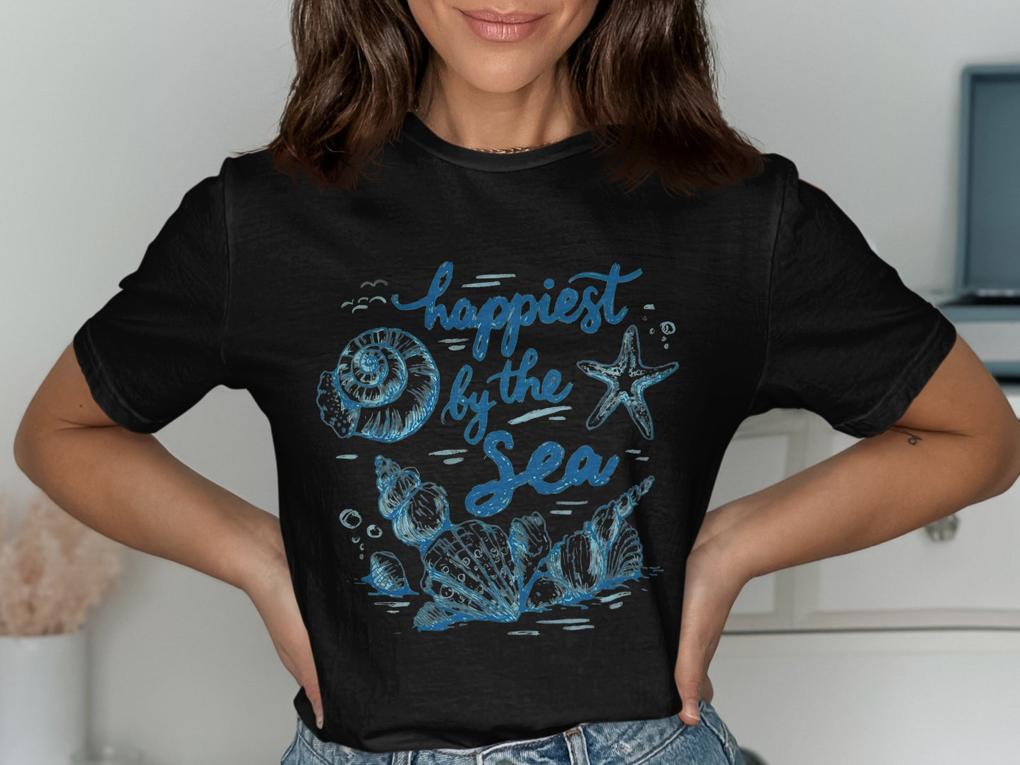Black t-shirt with blue "Happiest by the Sea" text and shell graphics.