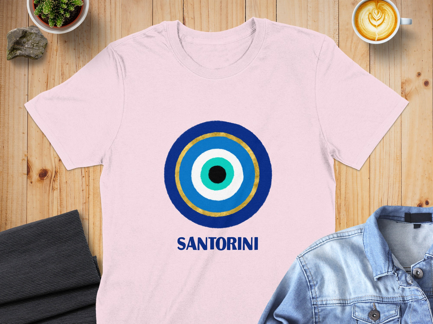 Pink t-shirt with a blue and gold evil eye design and "SANTORINI" text.