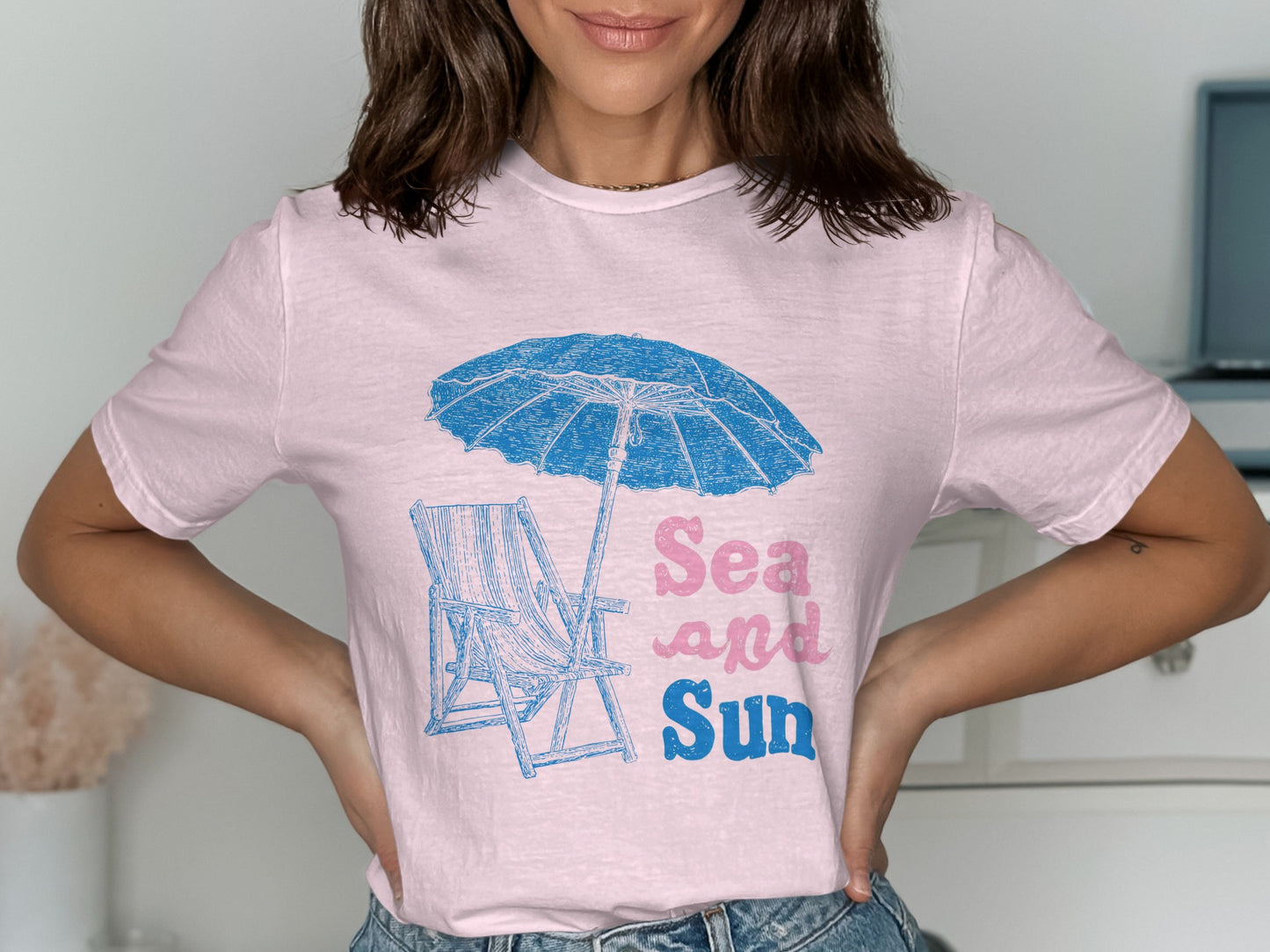 Pink t-shirt with blue beach umbrella, lounge chair, and "Sea and Sun" text.