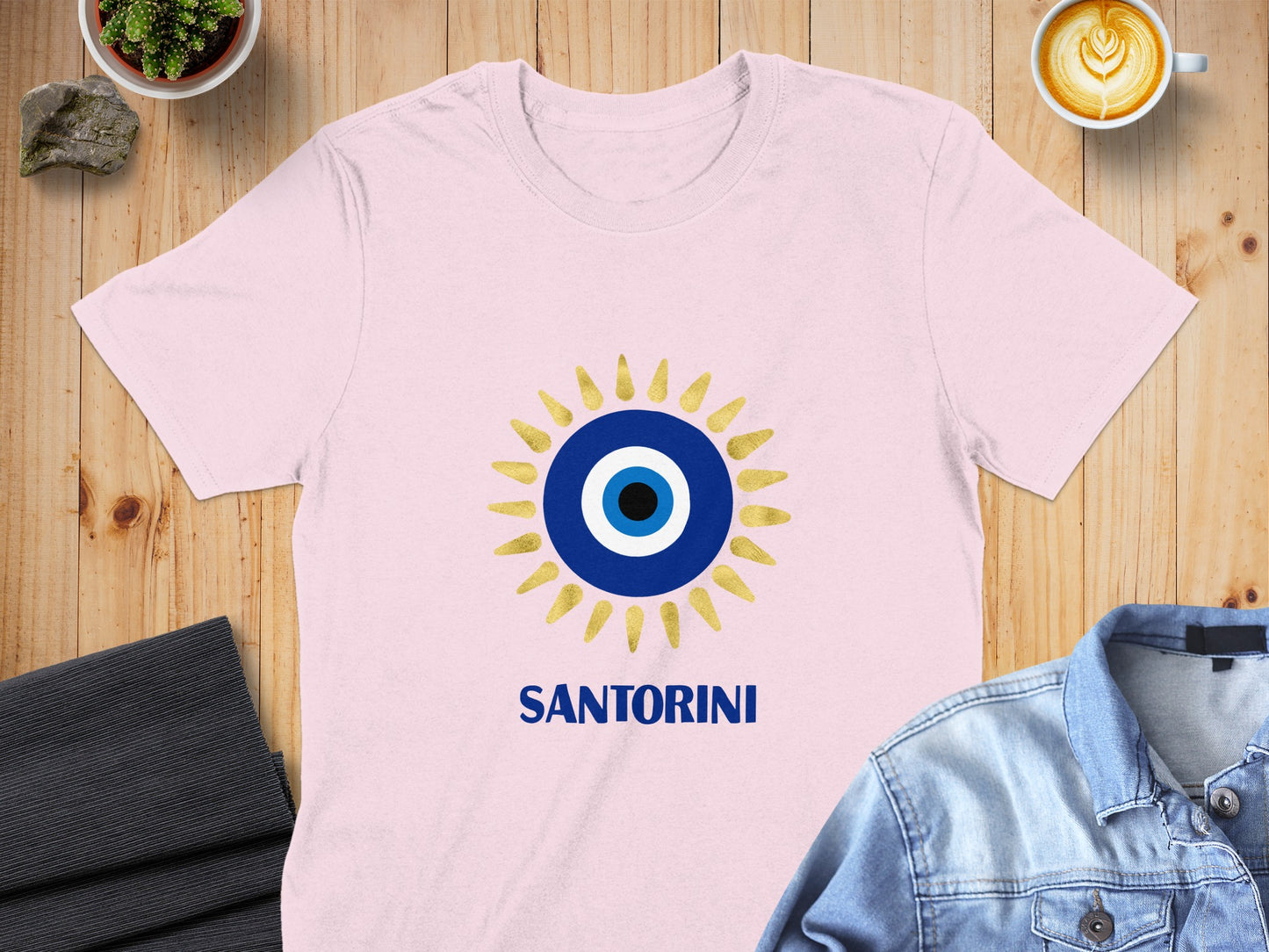 Pink t-shirt with a gold and blue evil eye design and "SANTORINI" text.