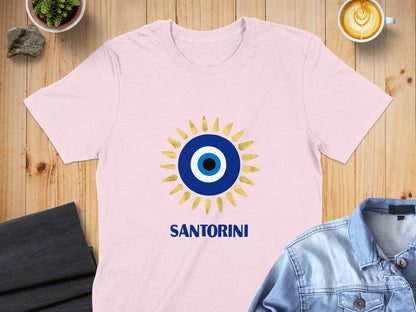 Pink t-shirt with a gold and blue evil eye design and "SANTORINI" text.