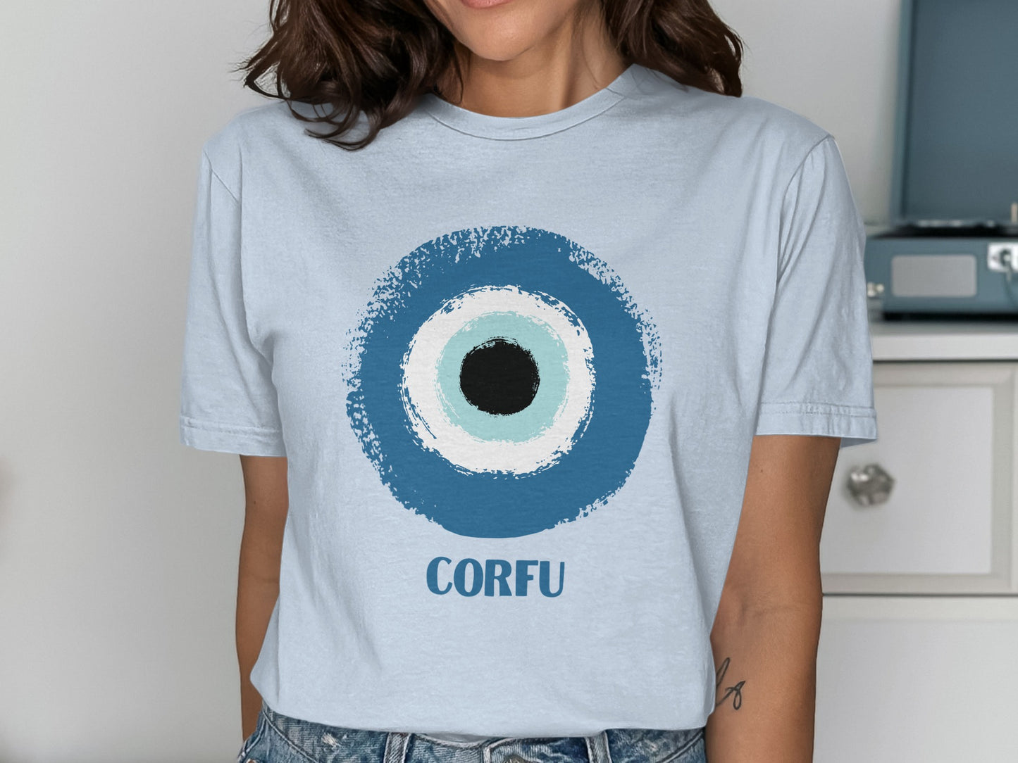 Light blue t-shirt with a blue, white, and black evil eye design and "CORFU" text.