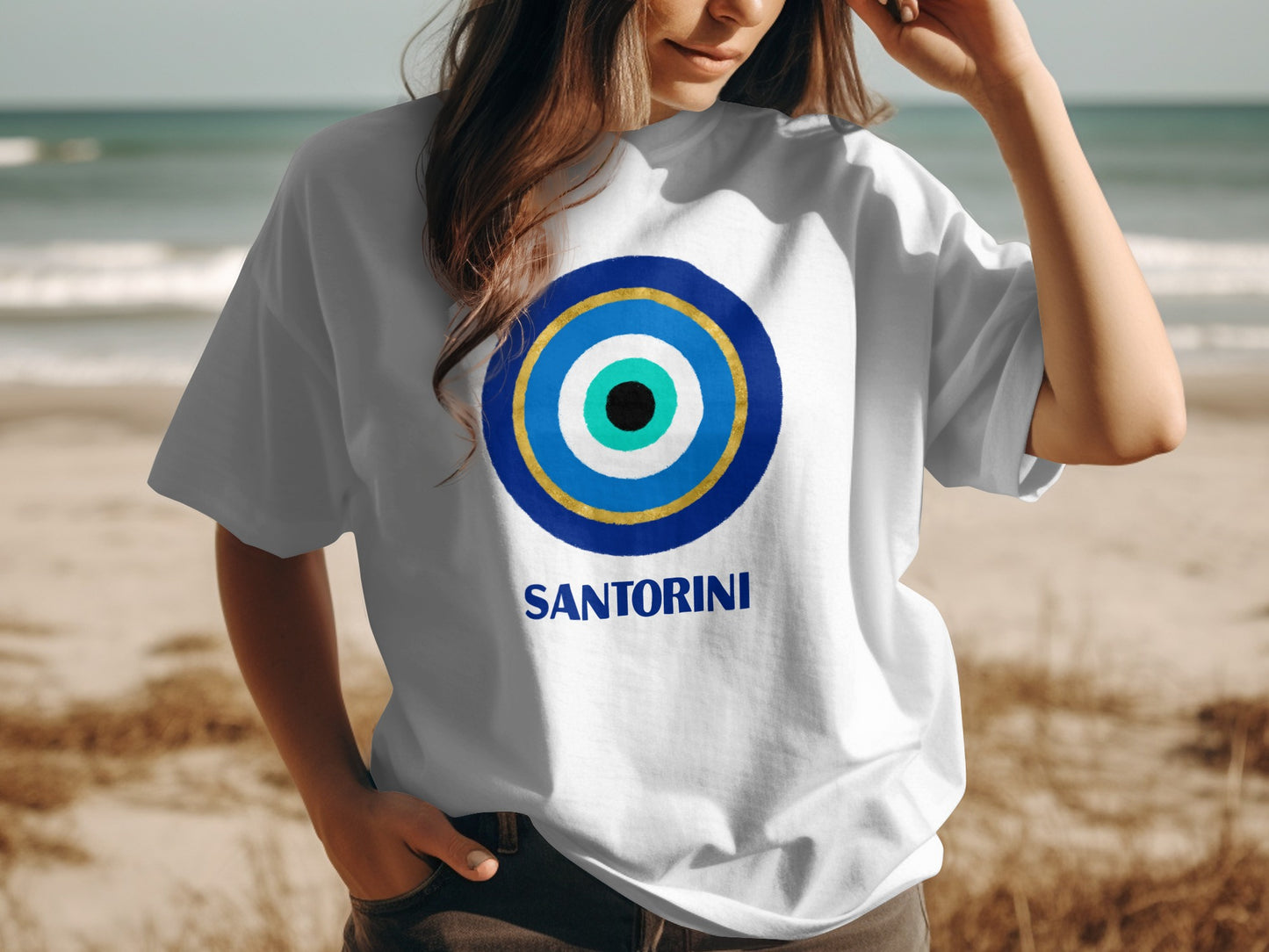 White t-shirt with blue and gold evil eye design and "Santorini" text.