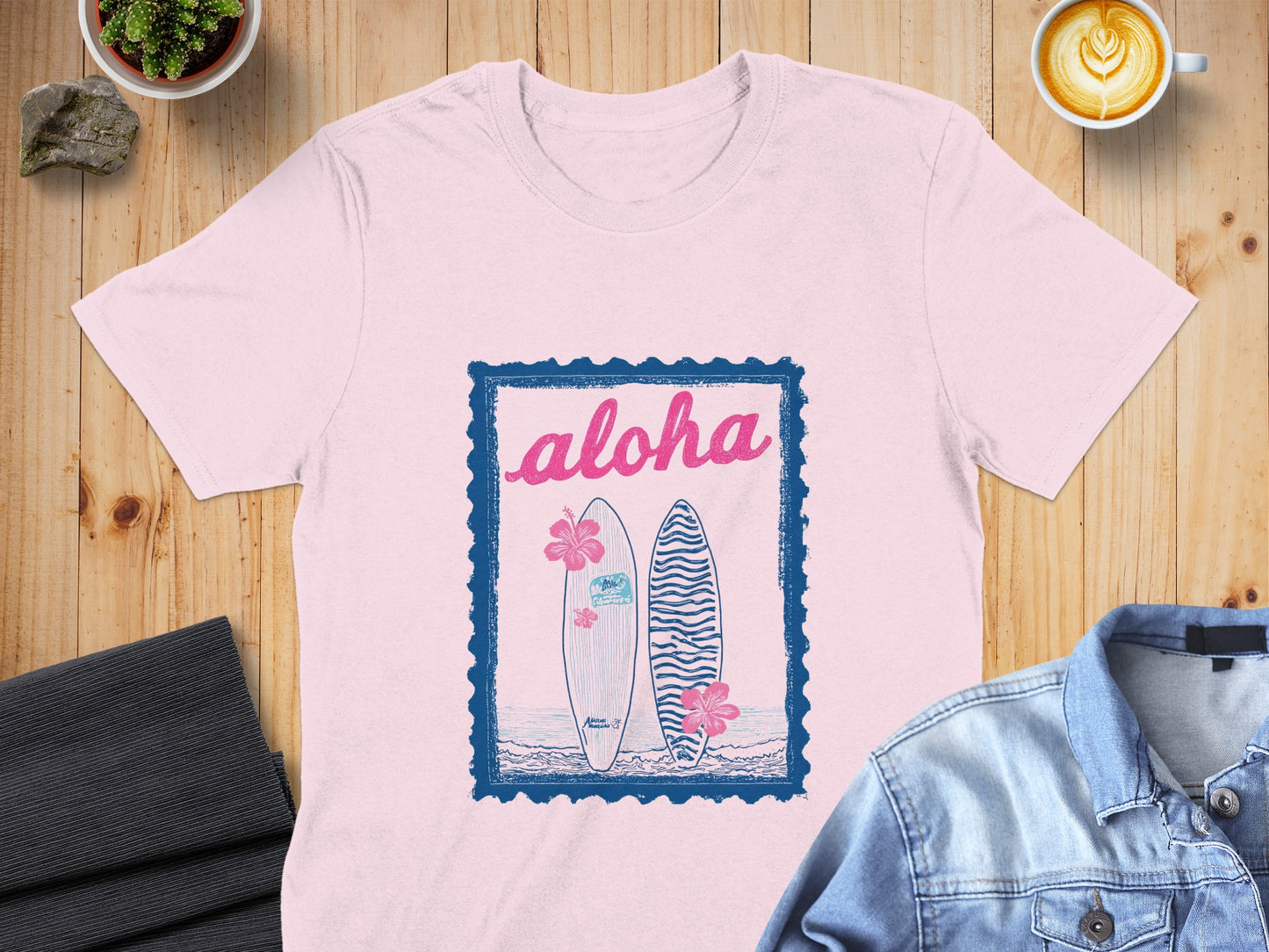 Pink t-shirt with blue "aloha" text, surfboards, and hibiscus flowers.