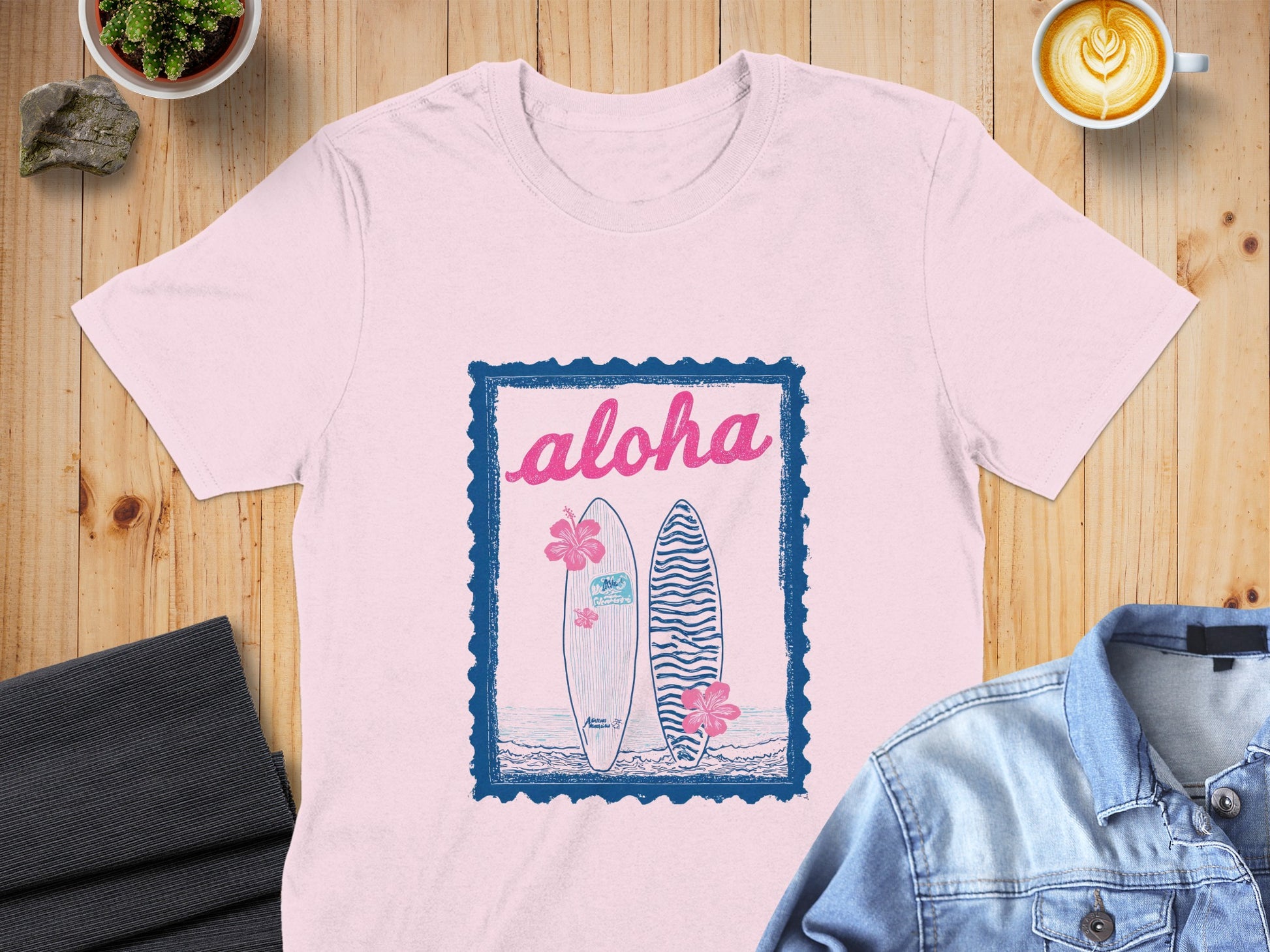 Pink t-shirt with blue "aloha" text, surfboards, and hibiscus flowers.