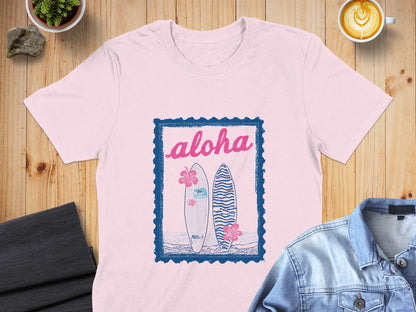 Pink t-shirt with blue "aloha" text, surfboards, and hibiscus flowers.