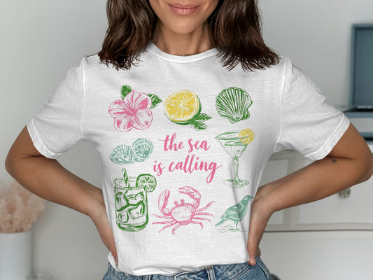 White t-shirt with "the sea is calling" text and tropical illustrations.