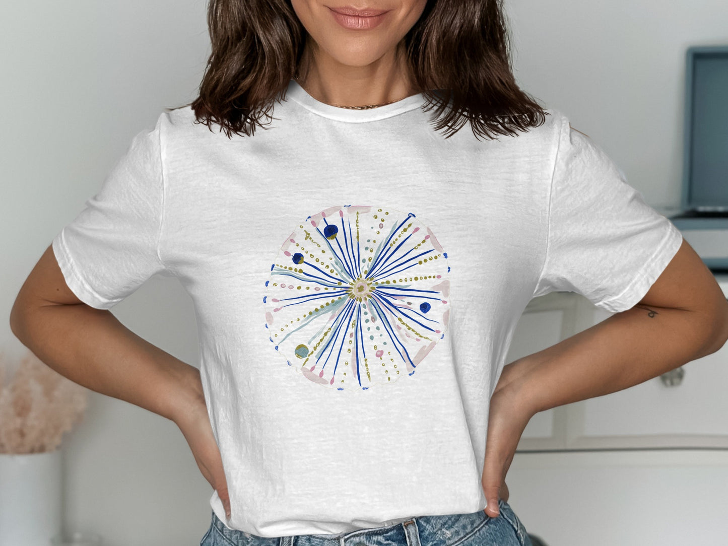 White t-shirt with a circular, starburst-like design in pink, blue, and gold.