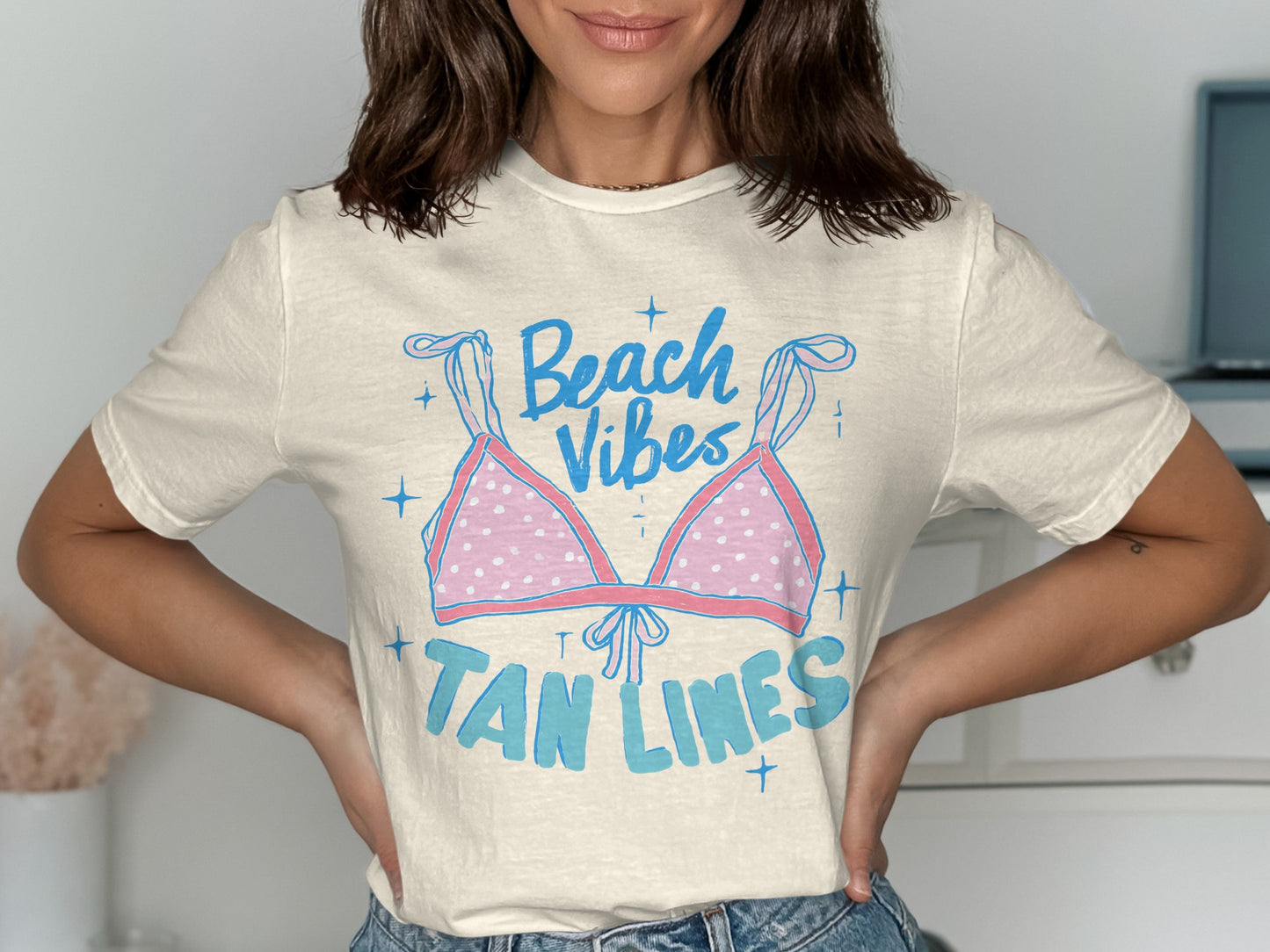 Cream t-shirt with "Beach Vibes Tan Lines" graphic featuring a pink polka dot bikini top.