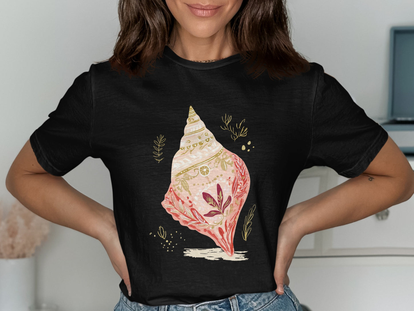 Black t-shirt with a decorated seashell and leaves graphic.