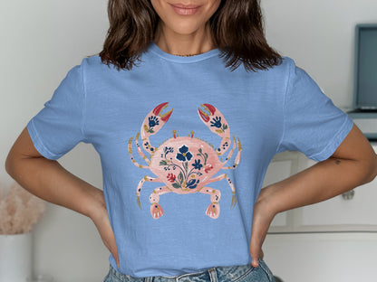 Light blue t-shirt with a pink crab graphic adorned with blue and gold floral details.