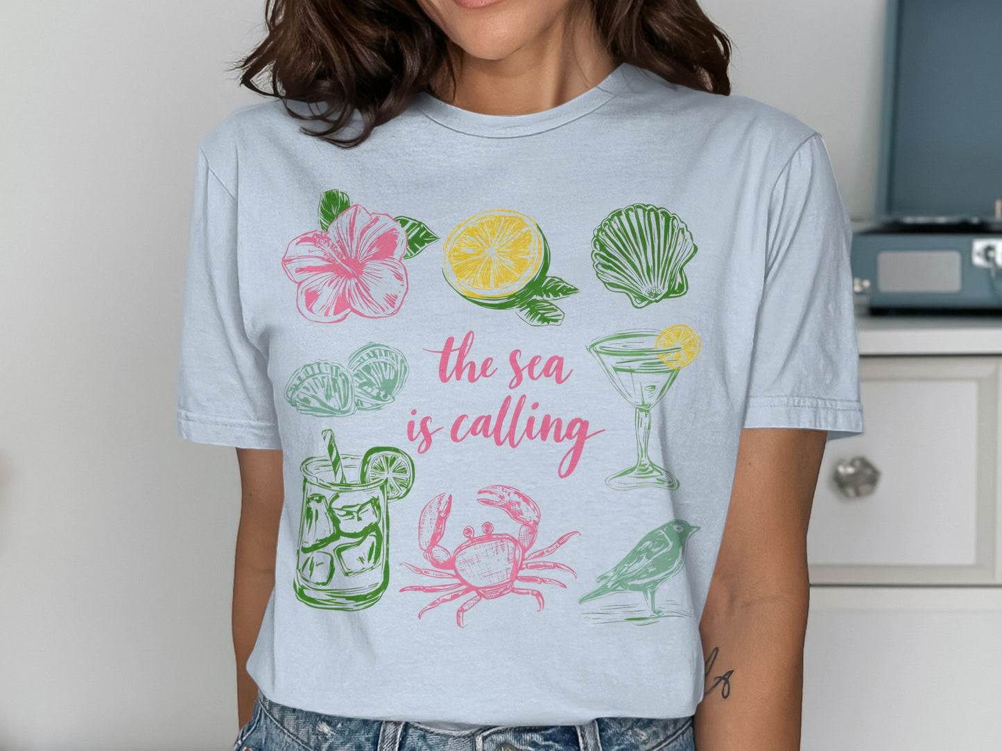 T-shirt featuring tropical and beach-themed illustrations and text: "The sea is calling".