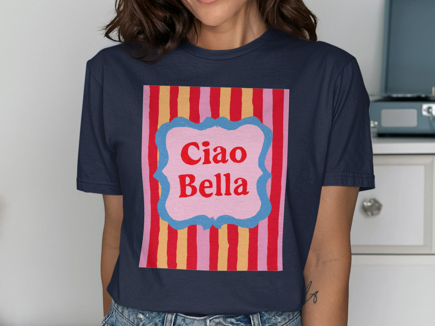 Navy t-shirt with "Ciao Bella" in a pink banner on a striped background.