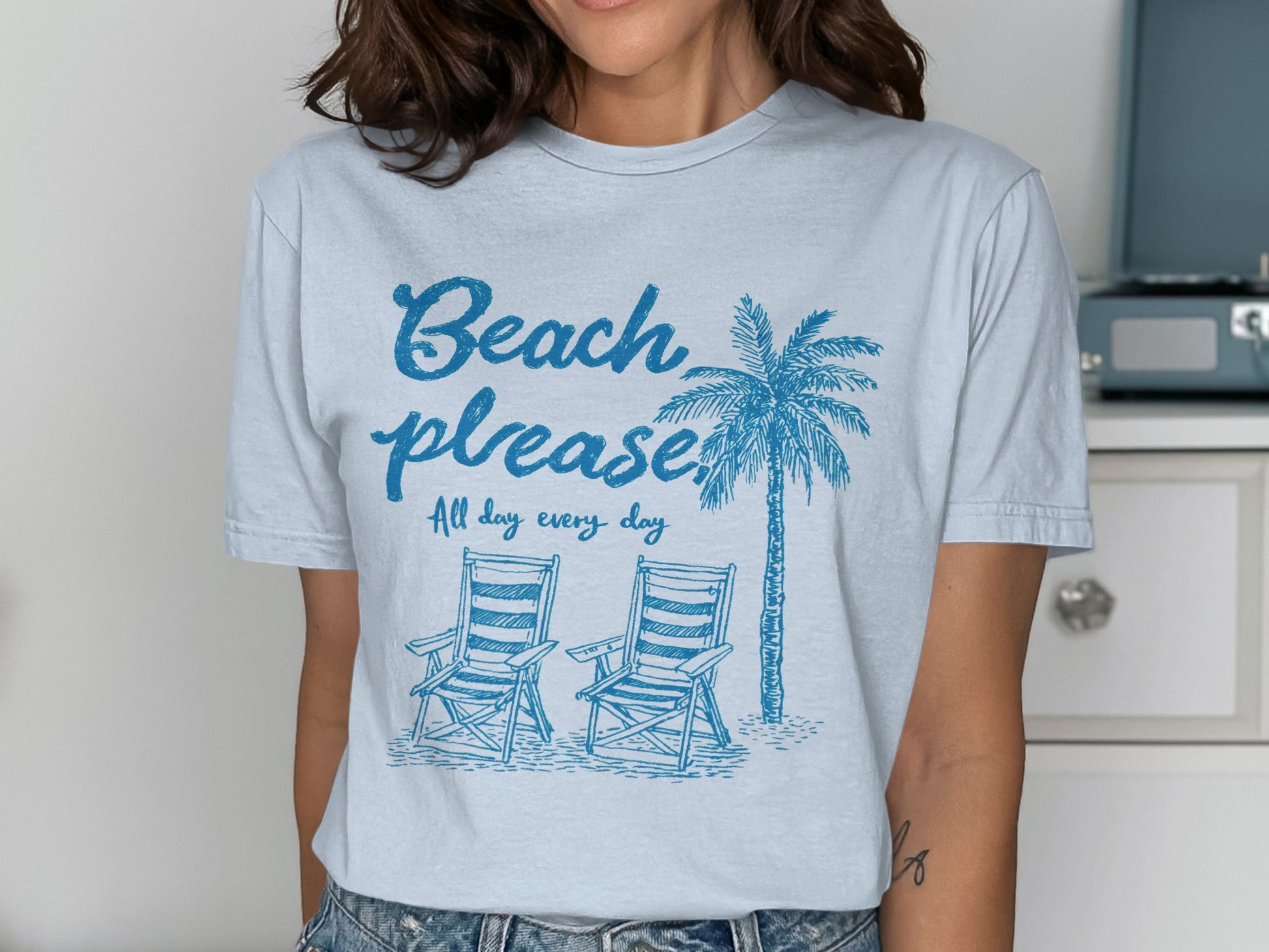 Light blue t-shirt with "Beach please" and palm tree, two beach chairs.
