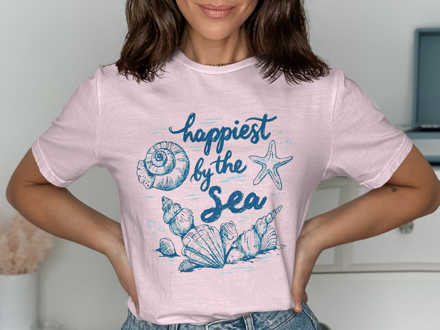 Light pink t-shirt with blue "Happiest by the Sea" text and seashell graphics.