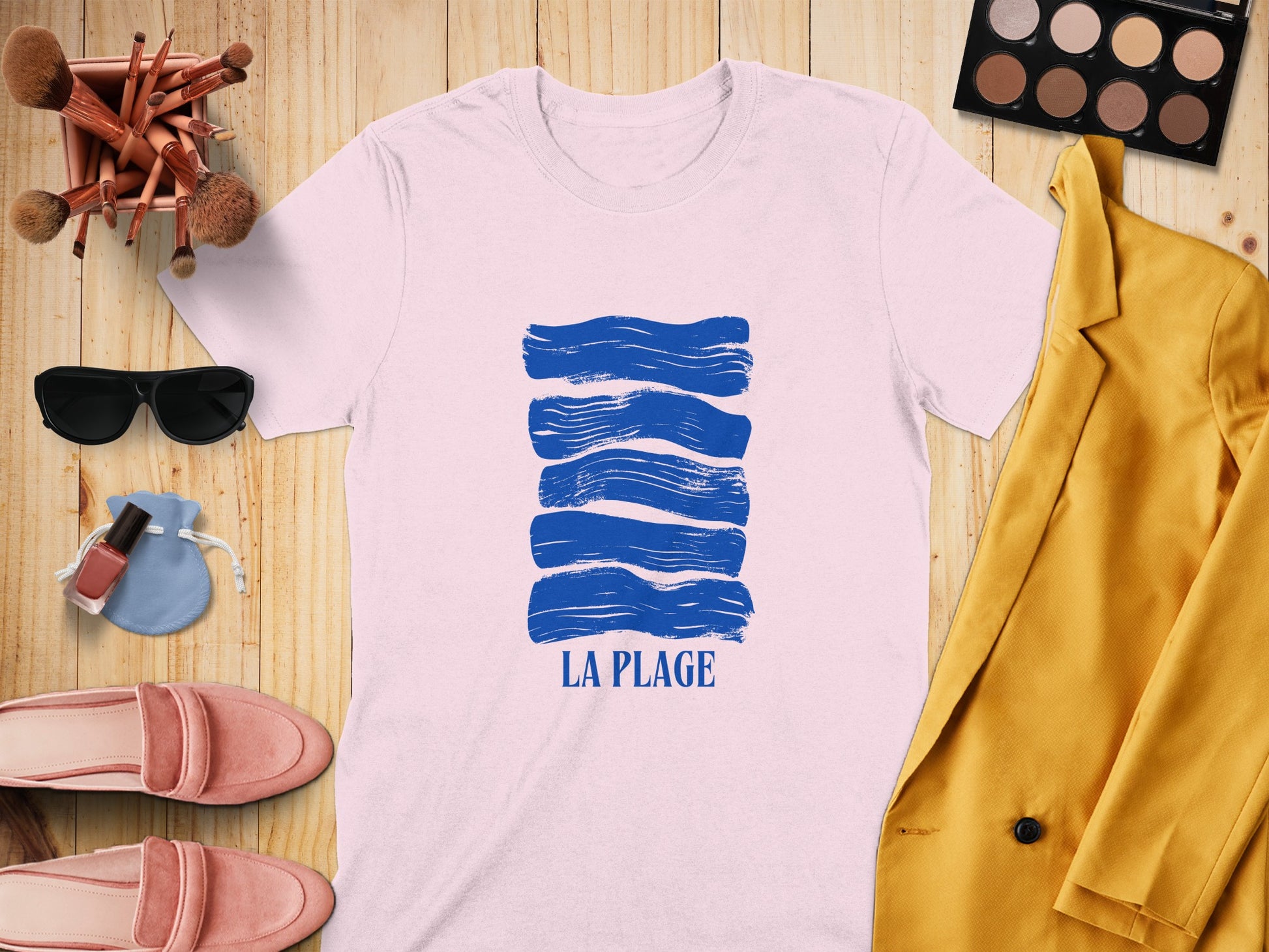 White t-shirt with blue wavy lines and "LA PLAGE" text, arranged with accessories.