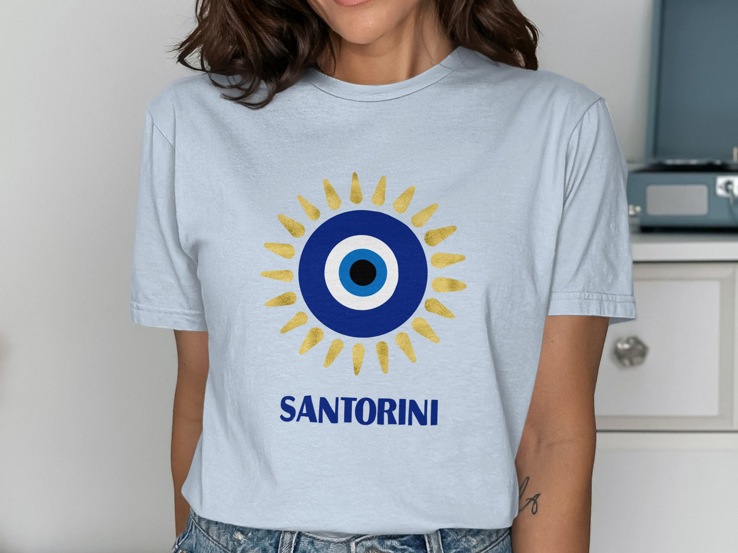 Light blue t-shirt with golden sun and Santorini evil eye design.