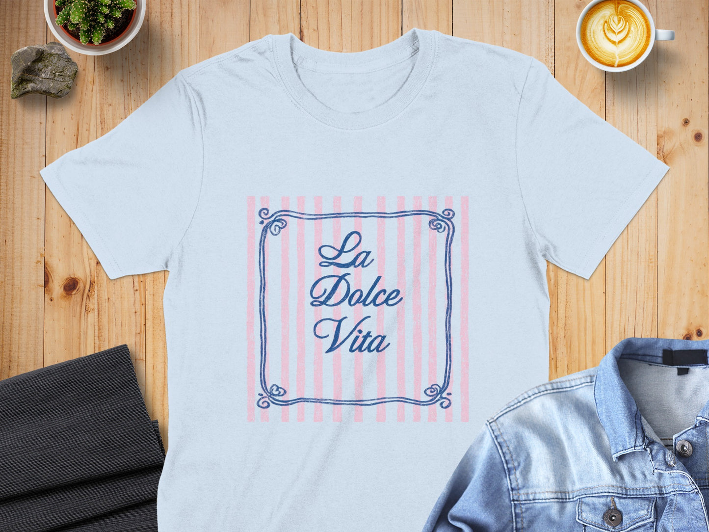 Light blue t-shirt with "La Dolce Vita" text in a decorative frame on pink stripes.