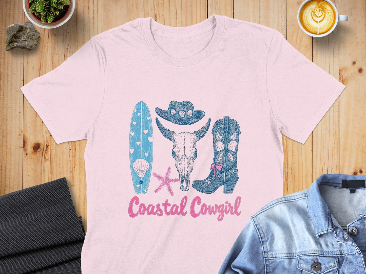 Pink t-shirt with coastal cowgirl graphic: surfboard, skull, cowboy hat, boots.