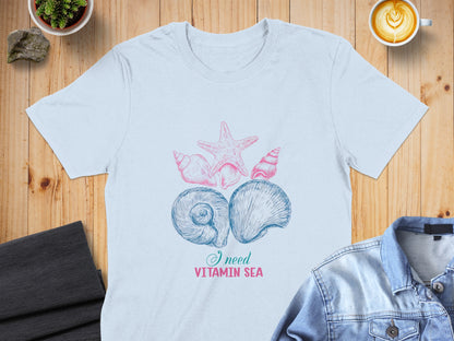 Light blue t-shirt with pink and blue seashell and starfish graphic and "I need vitamin sea" text.
