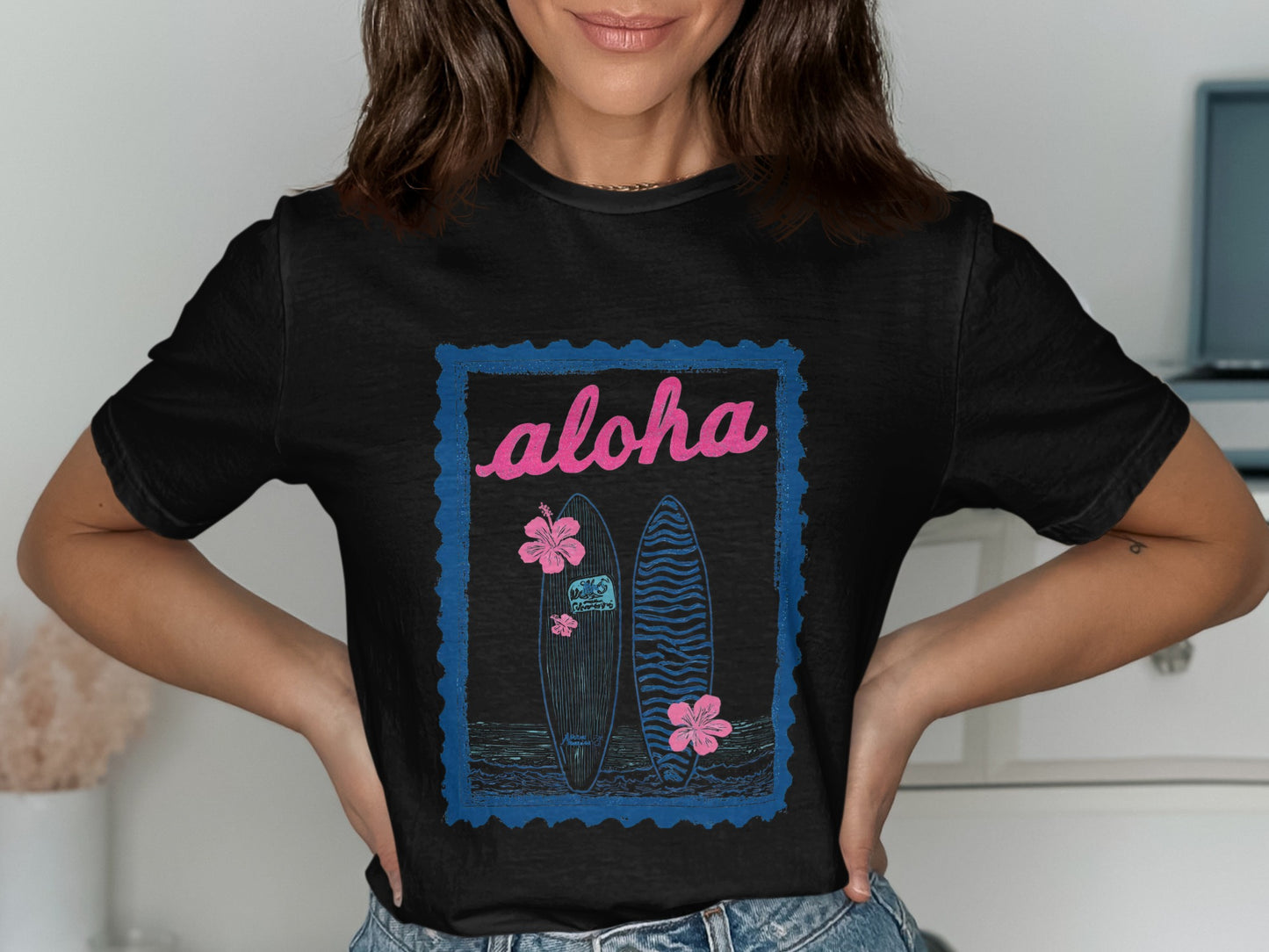 Black t-shirt featuring two surfboards, hibiscus flowers, and "Aloha" text within a stamp outline.