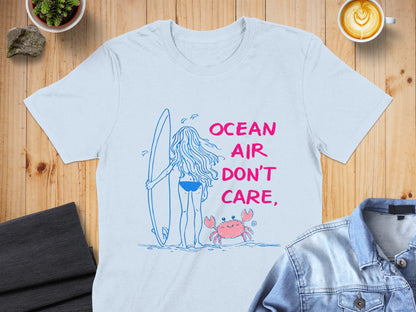 Blue t-shirt with a graphic of a person with a surfboard and a crab, reading "Ocean Air Don't Care".