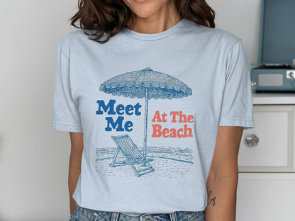 T-shirt with a beach scene featuring an umbrella and chair, and text "Meet Me At The Beach".