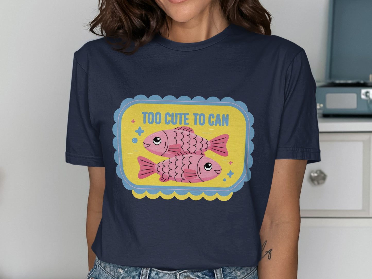 Navy t-shirt with a graphic of two pink fish and text that says "TOO CUTE TO CAN".