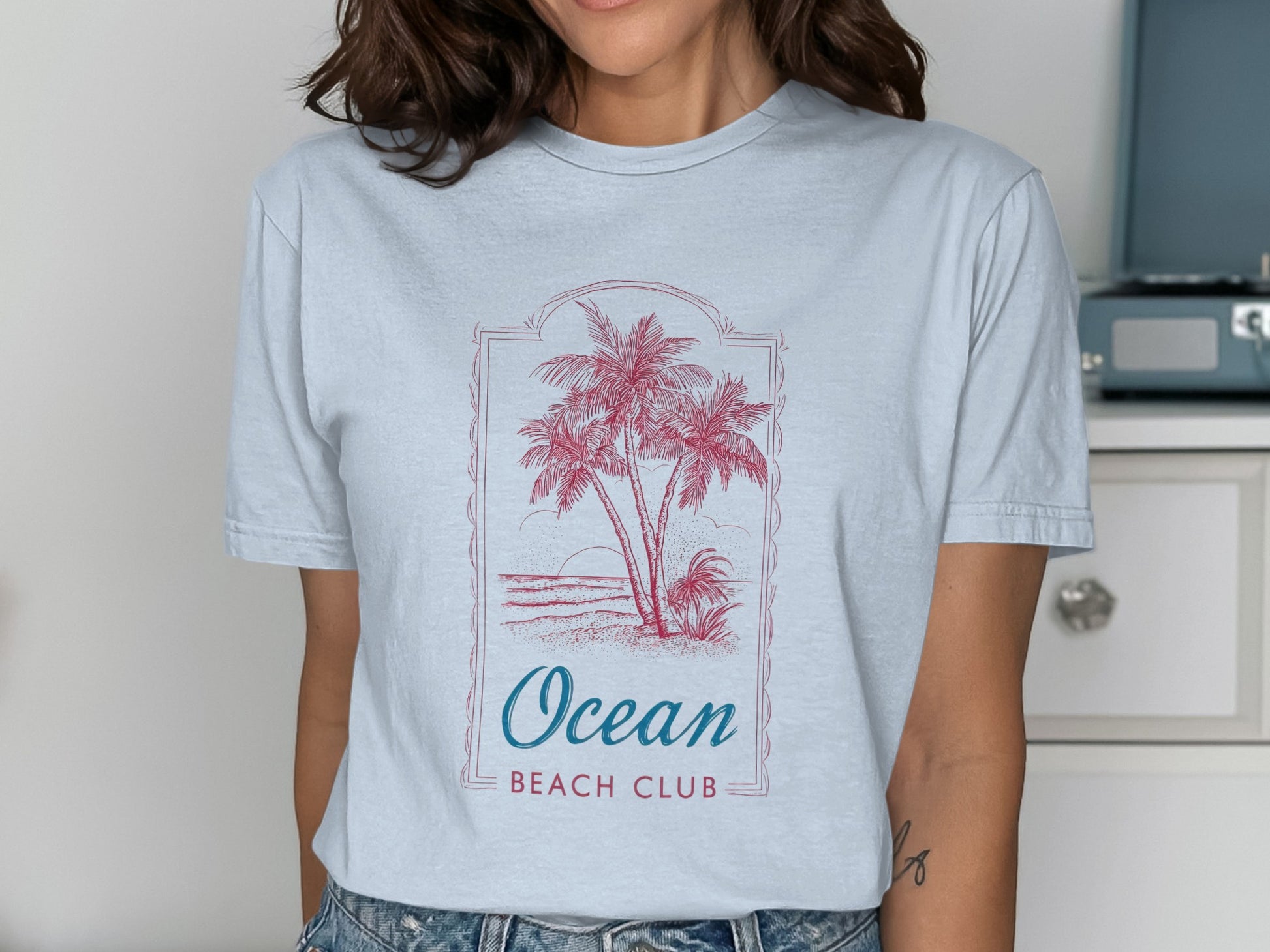 Light blue t-shirt with pink palm trees and "Ocean Beach Club" text.