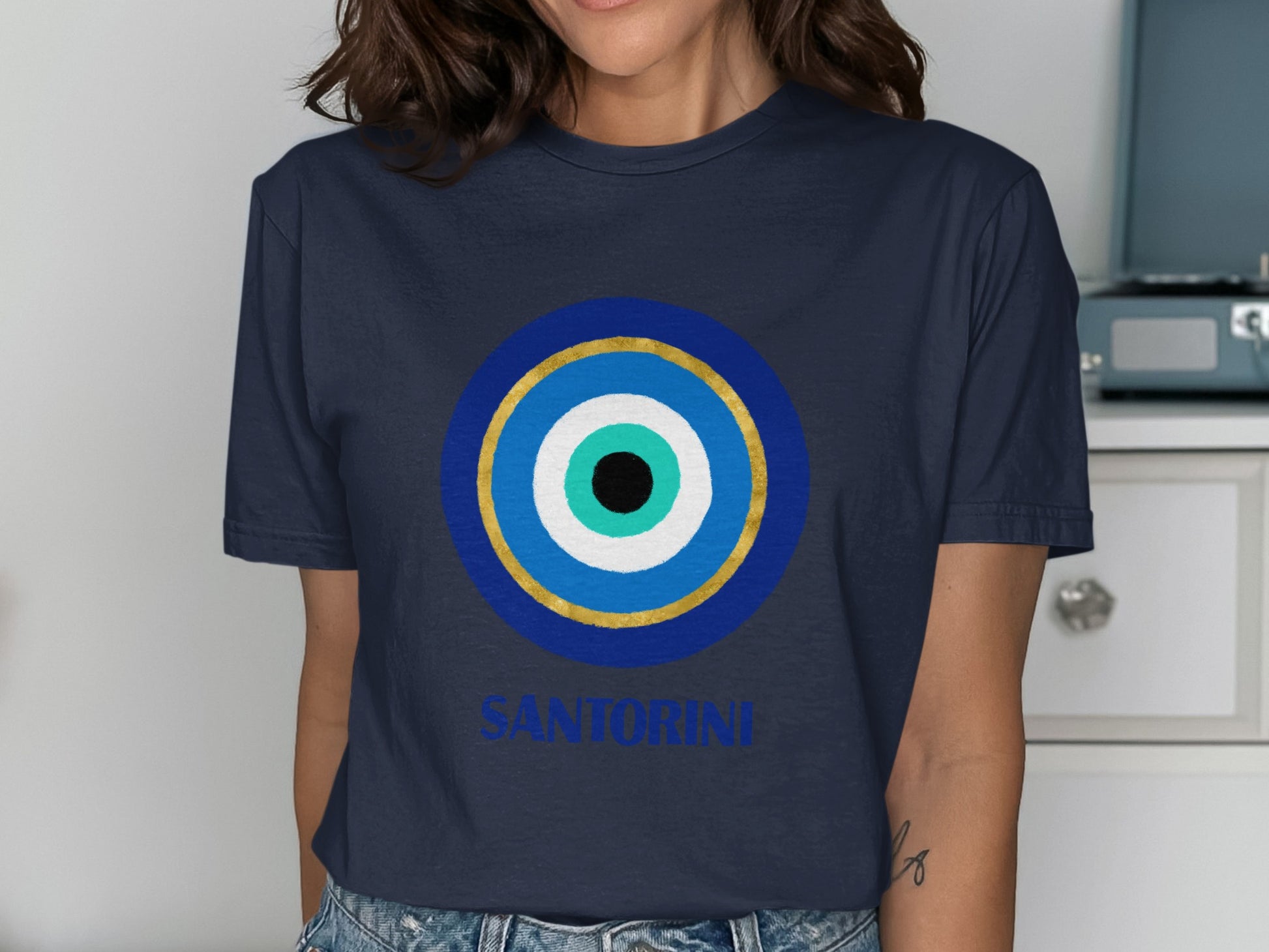 Navy t-shirt with a blue, white, and gold evil eye design and "Santorini" text.