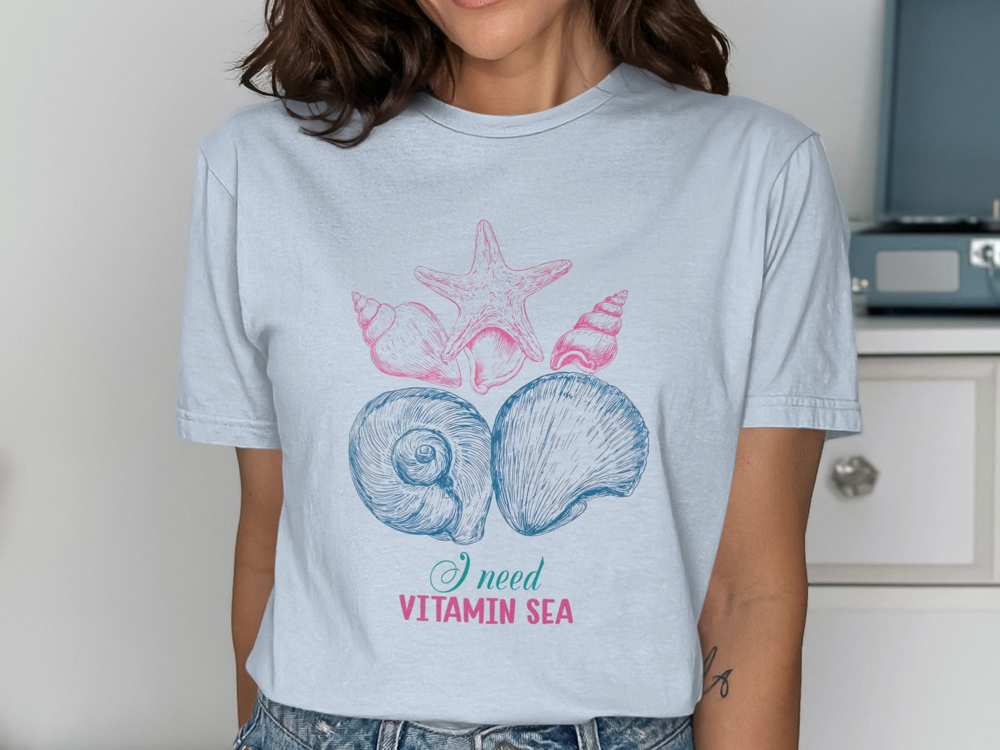 Light blue t-shirt with pink and blue shells and starfish graphic, reads "I need VITAMIN SEA".