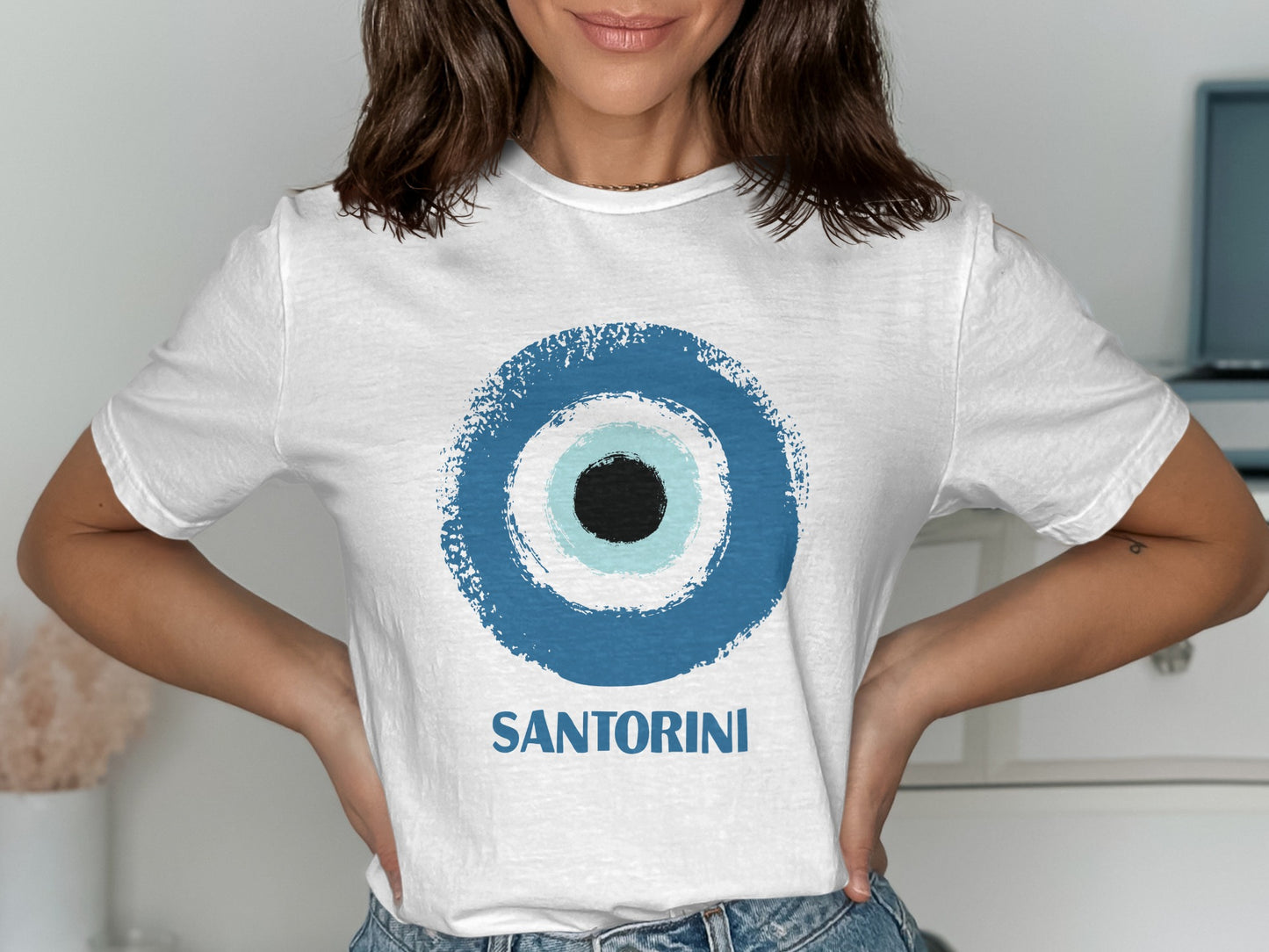 White t-shirt with a blue evil eye and "SANTORINI" text.