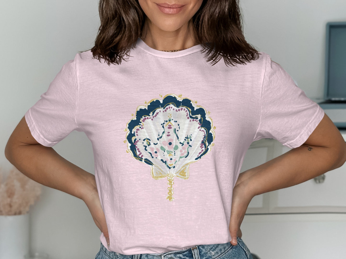 Pink t-shirt with a decorative fan and seashell graphic.