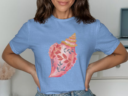 Light blue t-shirt with a watercolor illustration of a pink seashell adorned with floral branches.