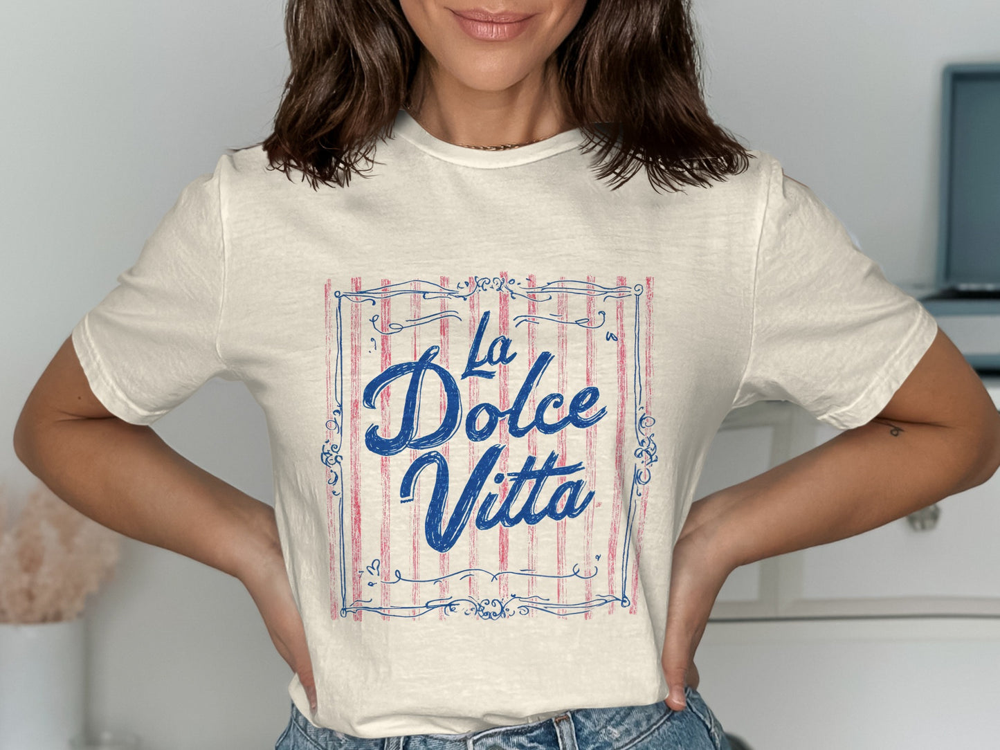 Cream t-shirt with "La Dolce Vita" in blue script on striped background.