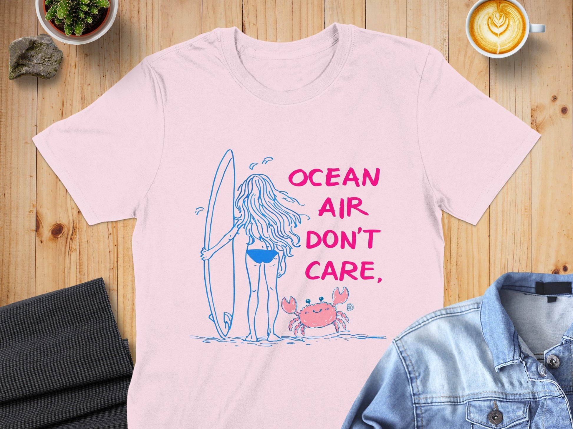 Pink t-shirt with "Ocean Air Don't Care" text and surfer girl with surfboard.