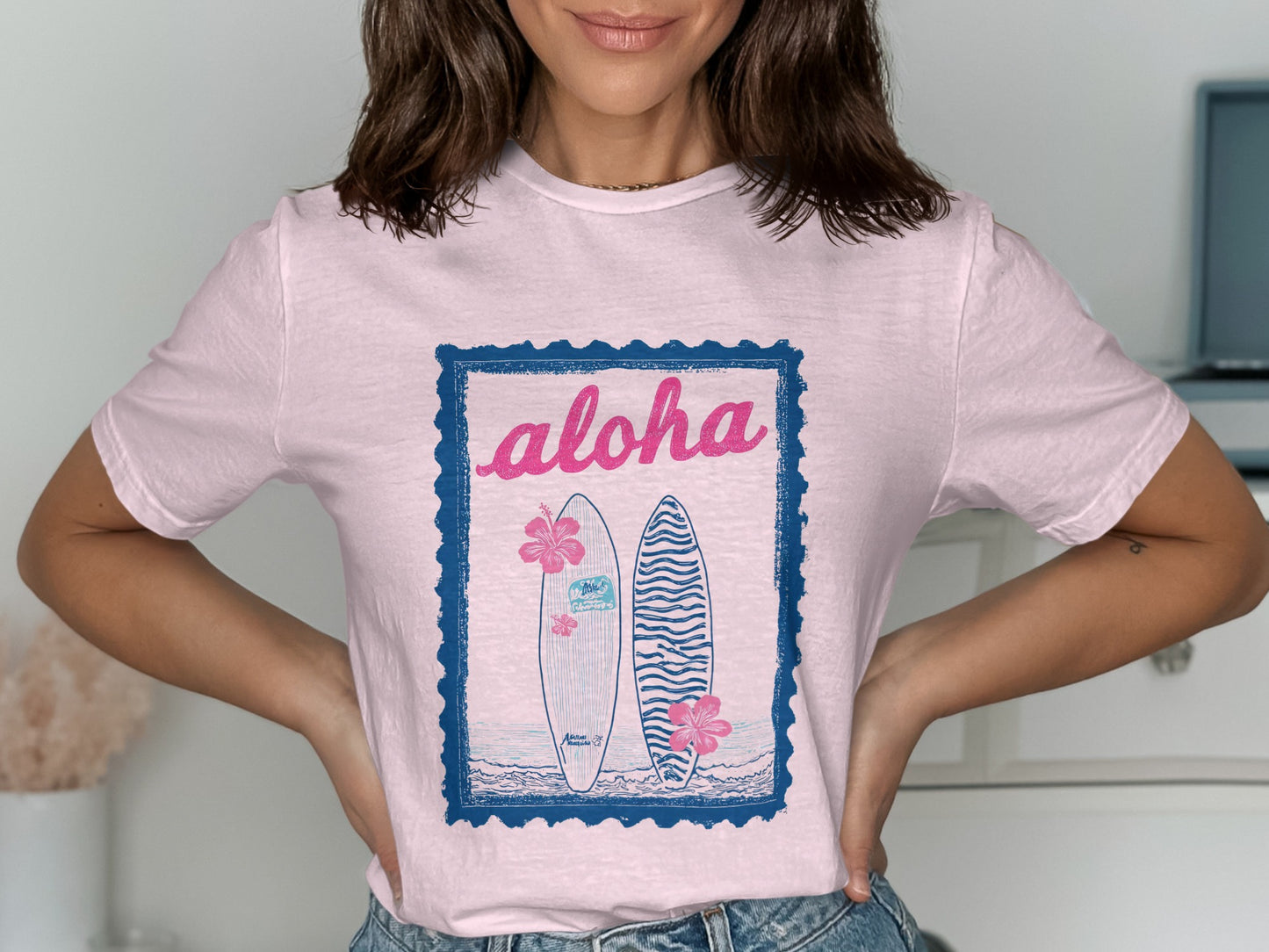 Pink t-shirt with "Aloha" and two surfboards graphic in blue frame.