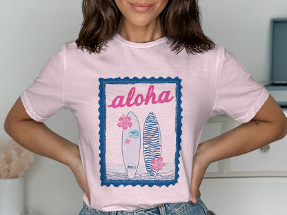 Pink t-shirt with "Aloha" and two surfboards graphic in blue frame.