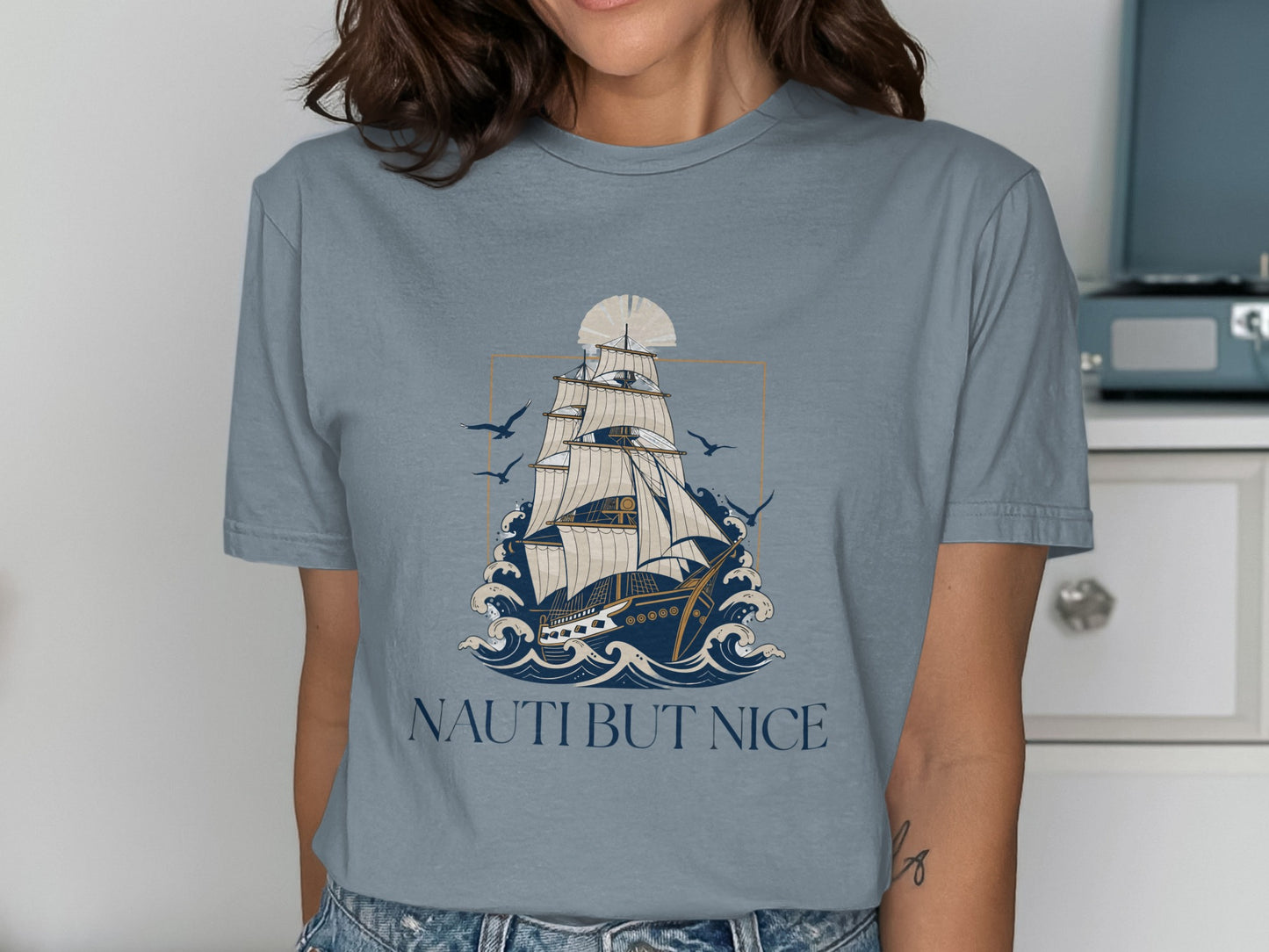 T-shirt graphic of a sailing ship on wavy water with birds and text NAUTI BUT NICE.