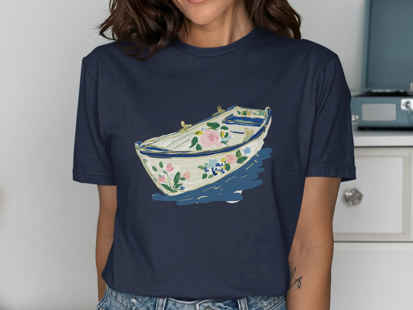 Navy t-shirt featuring a white boat with floral accents on blue water.