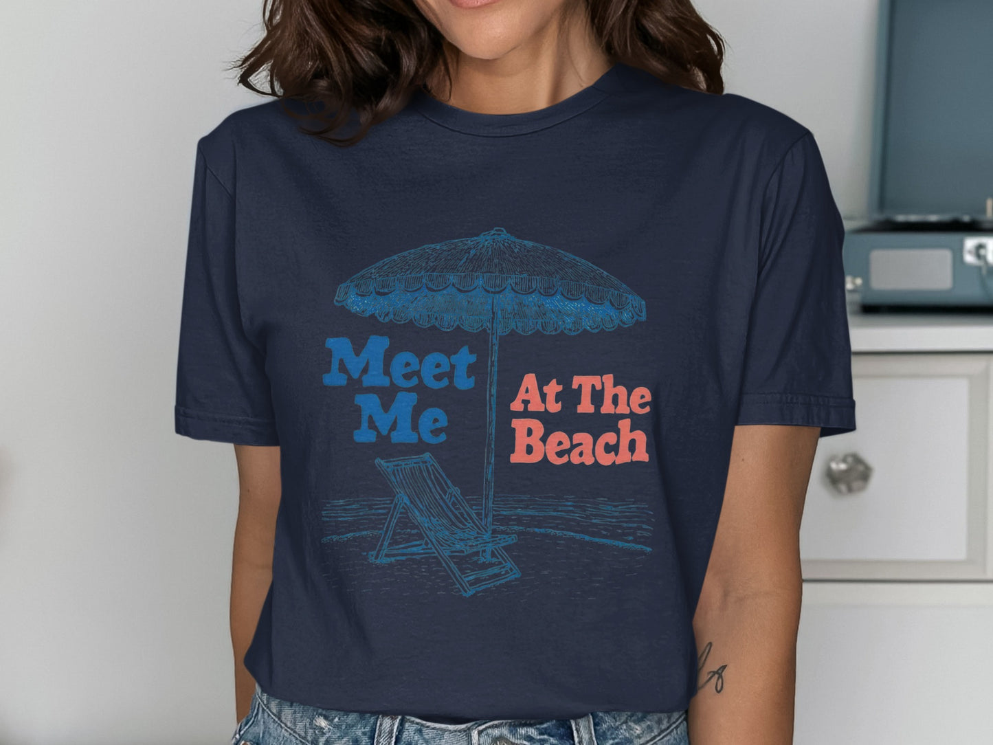 Navy t-shirt with "Meet Me At The Beach" text and beach scene illustration.