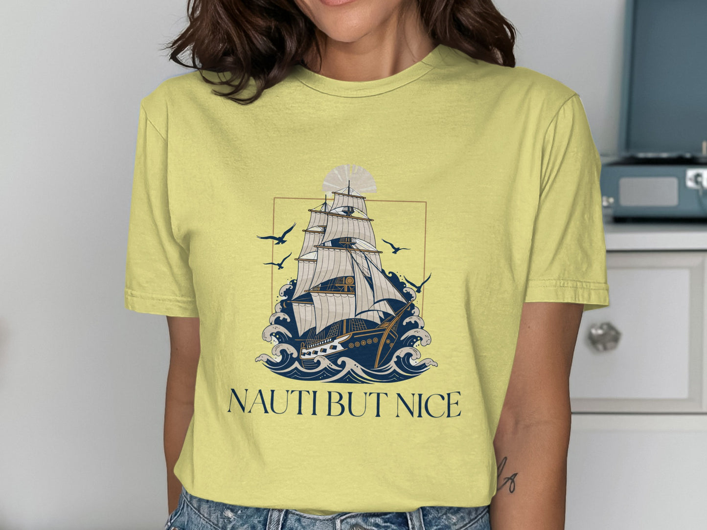 Yellow t-shirt with a sailing ship on wavy water and the text "NAUTI BUT NICE".