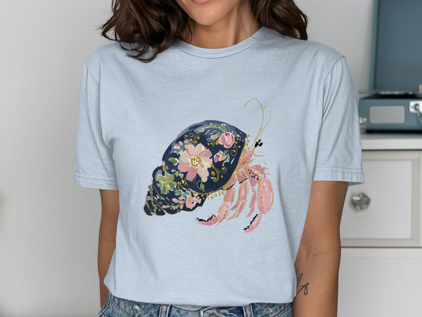 Light blue t-shirt featuring a watercolor hermit crab illustration with floral accents.