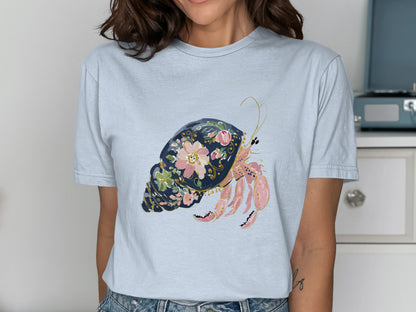 Light blue t-shirt featuring a watercolor hermit crab illustration with floral accents.