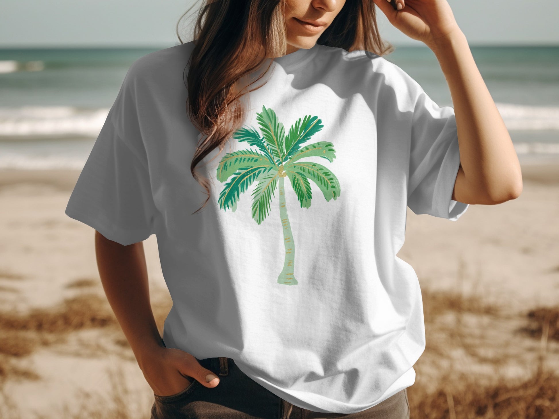 White t-shirt with a watercolor palm tree graphic on a beach.